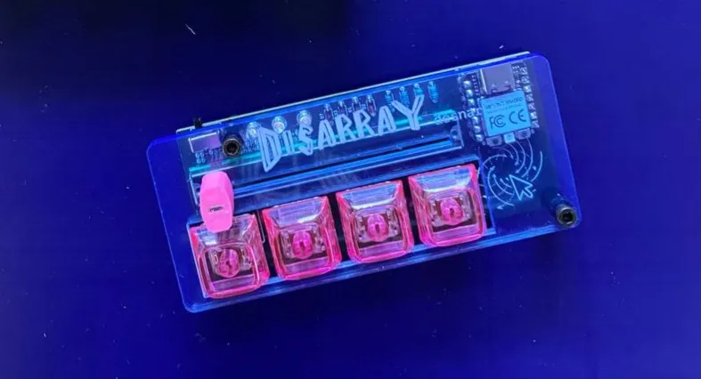 A Disarray Desnarler in a translucent blue acrylic case with four pink keycaps and a pink fader cap, under blue light.