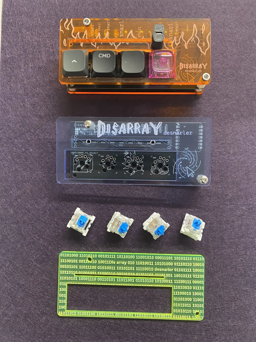 Desnarler parts laid out: an assembled orange unit, a bare board under a clear Disarray top plate, four blue switches and a neon green top plate engraved with binary.