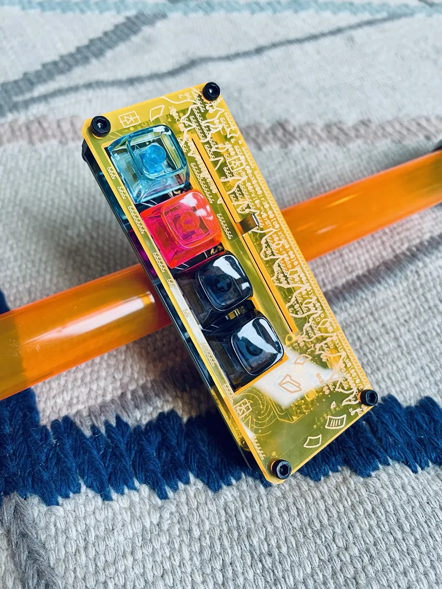 A Disarray Desnarler in a yellow acrylic case propped on an orange acrylic rod on a woven rug.