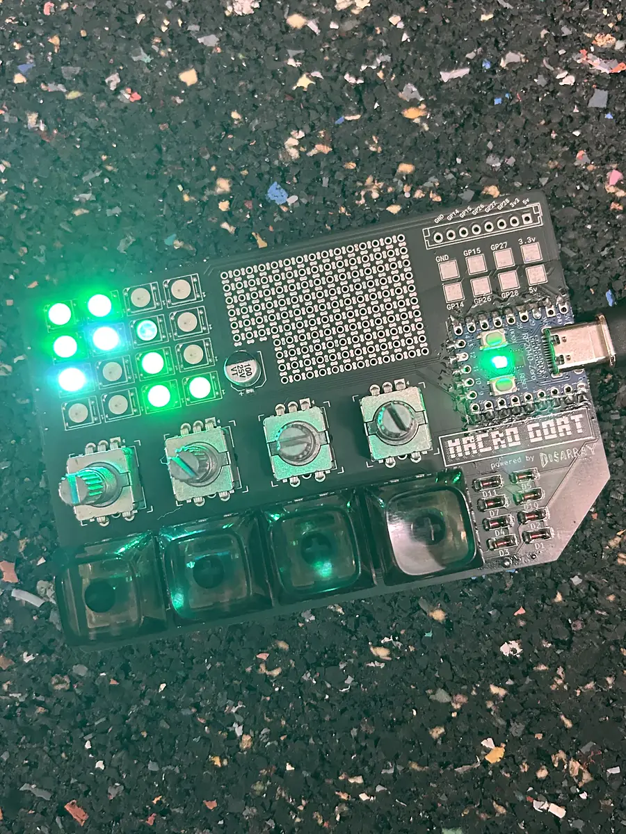 A macro_GOAT with four rotary encoders and clear keycaps, plugged in over USB-C, some of its LEDs glowing green, on a speckled rubber floor.