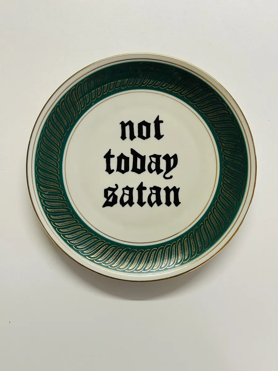 A white plate with a green and gold border, hand-lettered in black blackletter: not today satan.