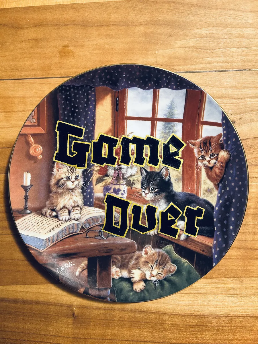 A collector plate painted with kittens by a window, lettered Game Over in black with a yellow outline.