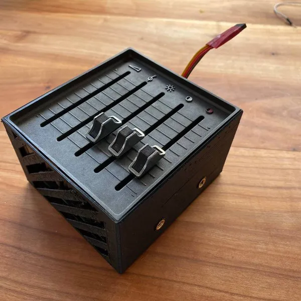 A black 3D-printed box topped with the TV's control panel: three slide potentiometers next to small icons, with a red and yellow cable coming out the back.